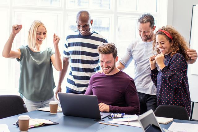 Fünf Personen in einem Büro feiern gemeinsam vor einem Laptop, sichtbar erfreut und motiviert
